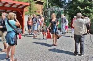 Tourists arriving at the Sierra Silver Mine Tour via a vintage green trolley, surrounded by trees and rustic buildings. Photo courtesy Wallace Chamber of Commerce.