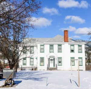 snow surrounds the white Staff House Museum building, trimmed with green