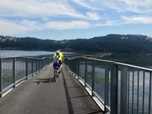 two people ride bikes on a bridge over a lake