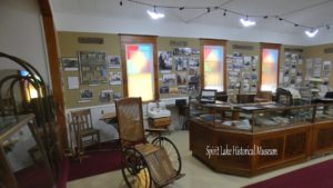 an indoor shot of a historic wheel chair and other items in Spirit Lake Historical Museum