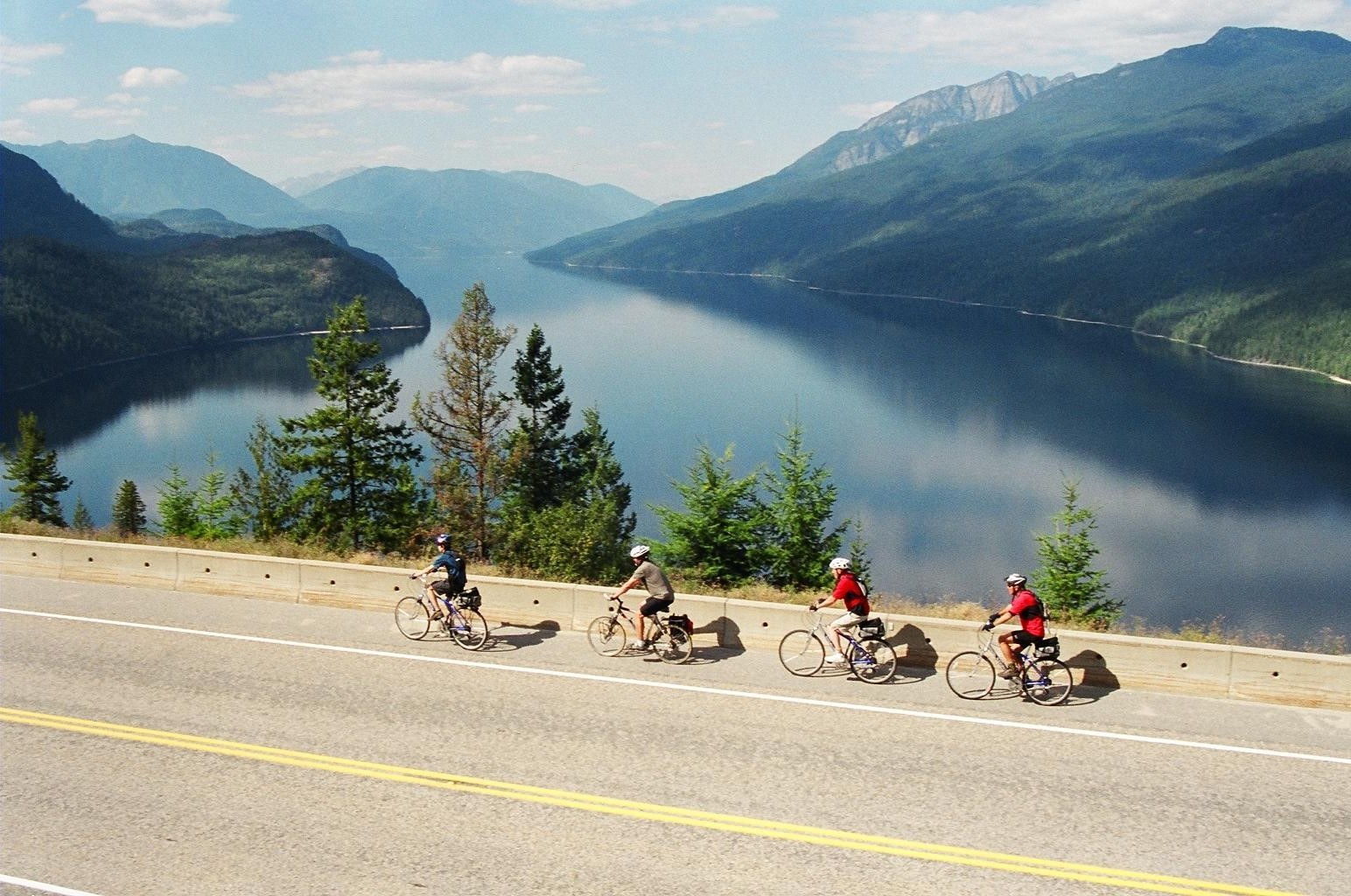 four cyclists bike along Highway 6 with an overlook of the lakes and mountains