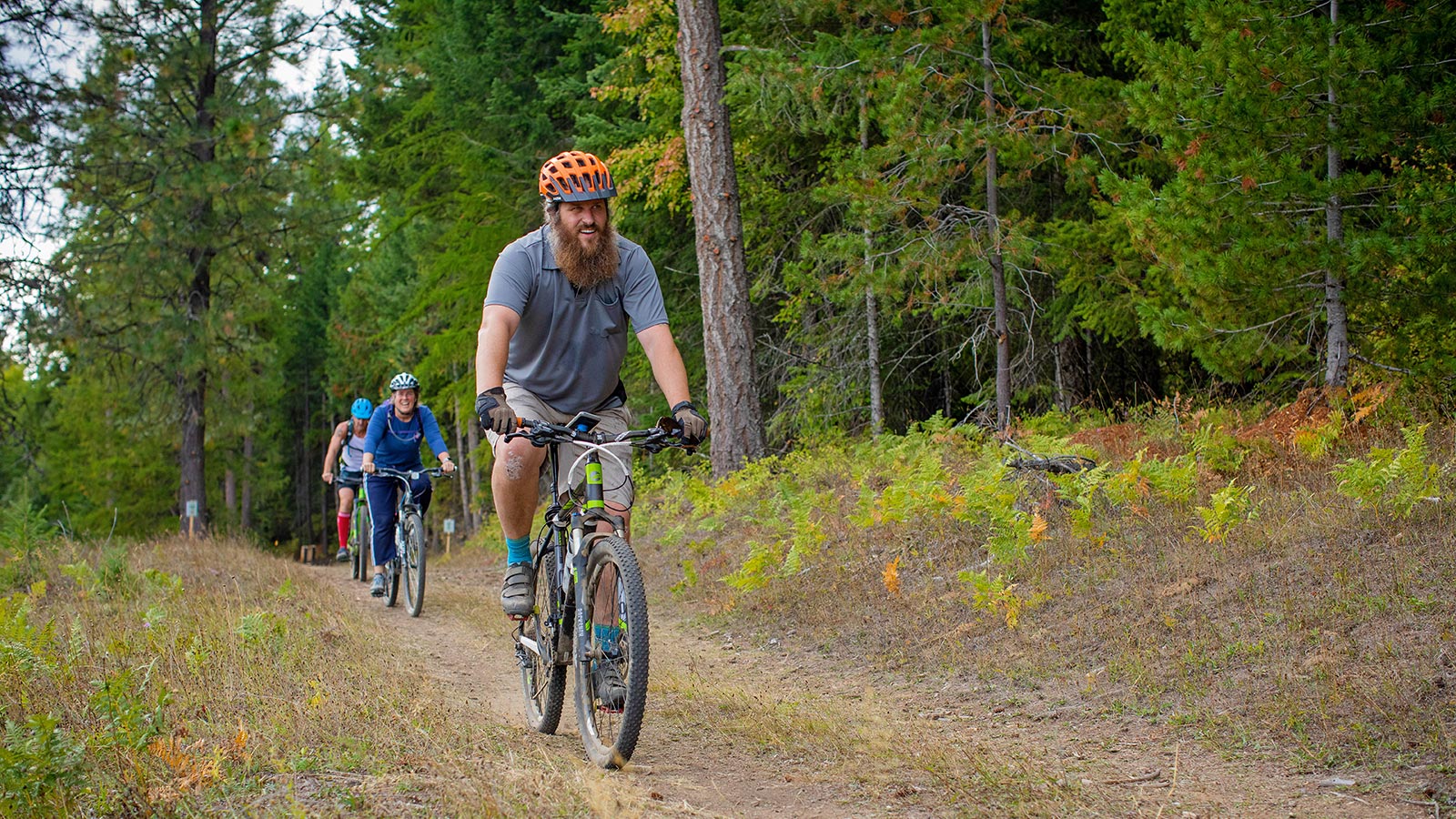 three people ride mountain bikes along a trail