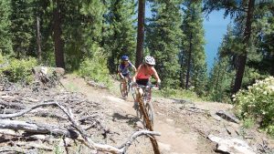women mountain biking through the trees on a dirt trail