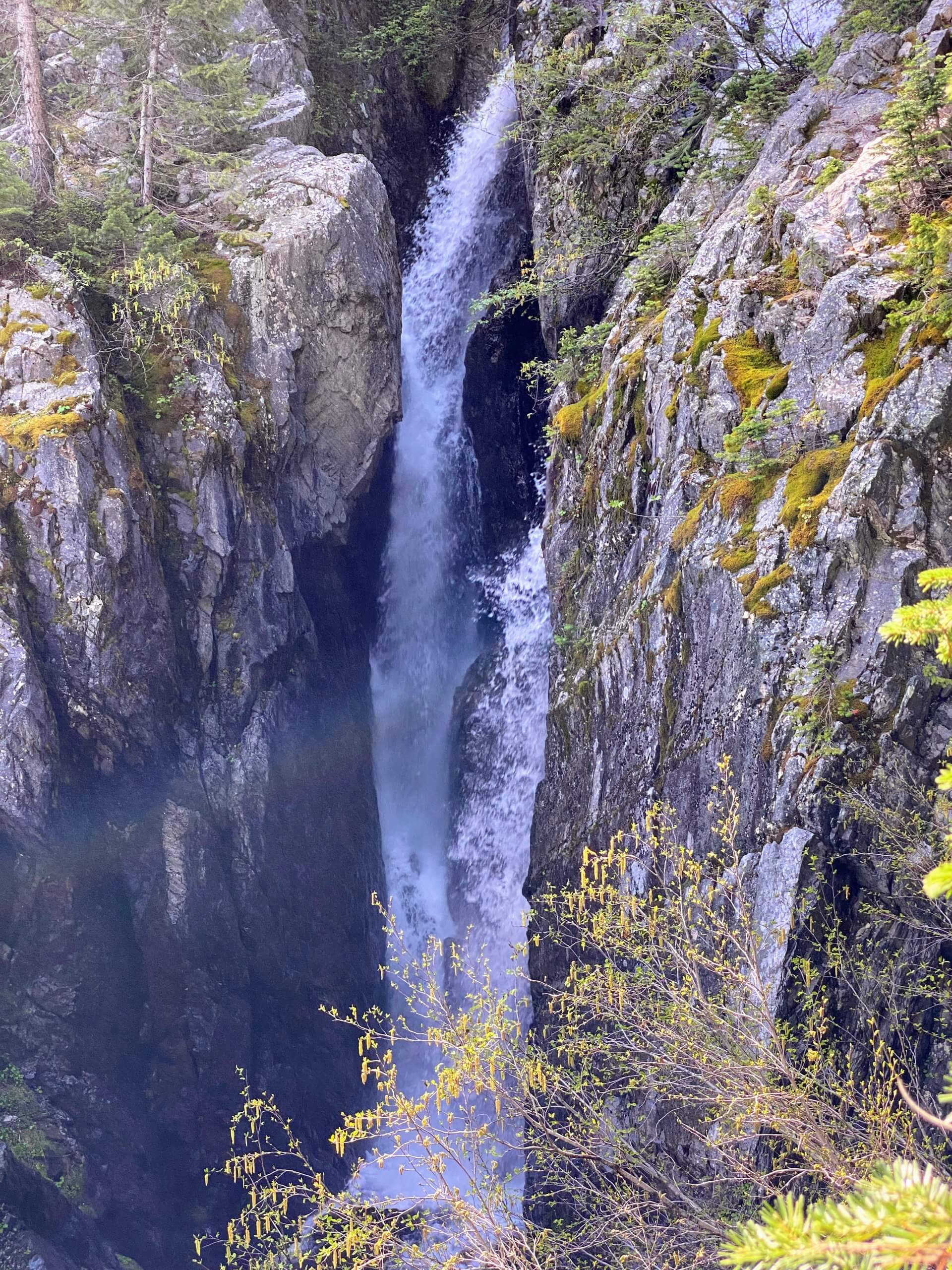 A view from the top of the Upper Stevens Lakes Falls as they cascade soaring down, splashing through moss and greenery from tall cliffs near Mullan, Idaho.