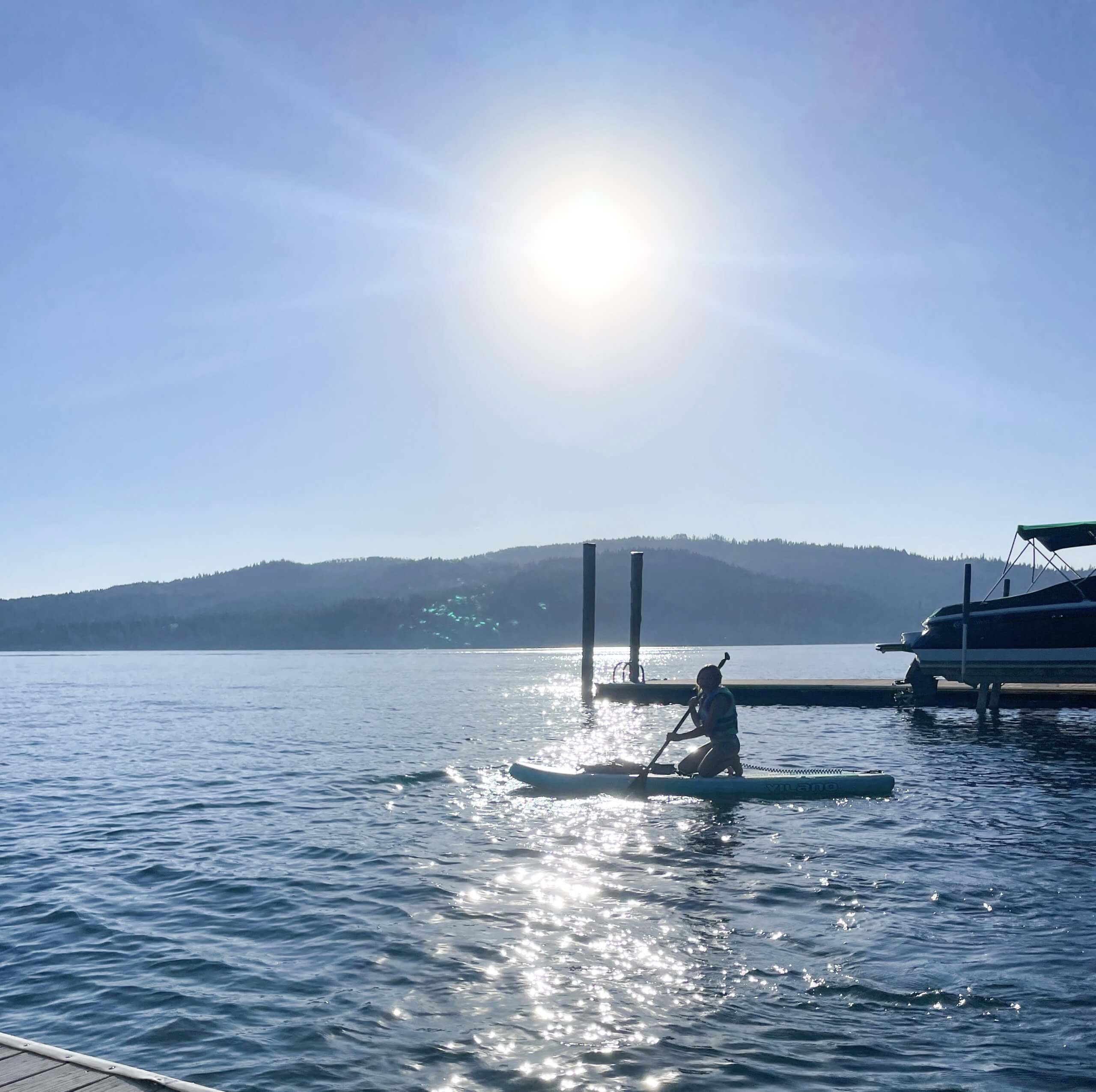 A person paddleboarding between boat docks on Lake Coeur d'Alene, and a docked boat in the background.