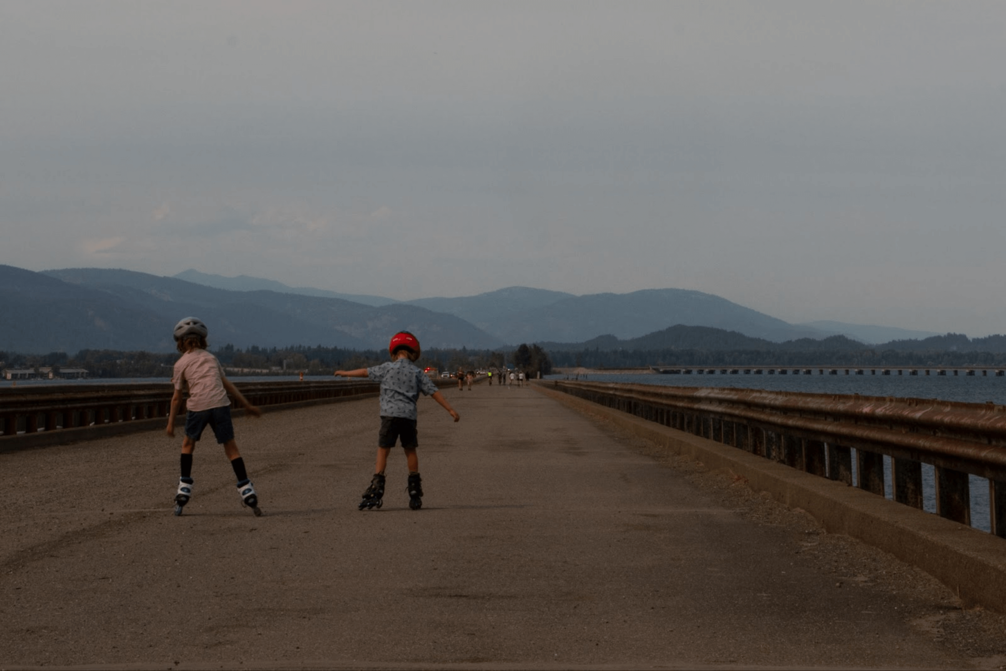 Two children rollerblading along the paved Long Bridge - Sagle Trail and several other people walking in the distance.