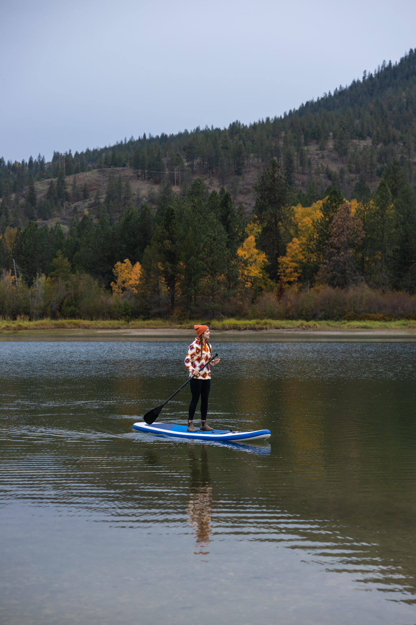 A person paddleboarding on the tree-lined Pend Oreille River at Riley Creek Recreation Area on a foggy day.