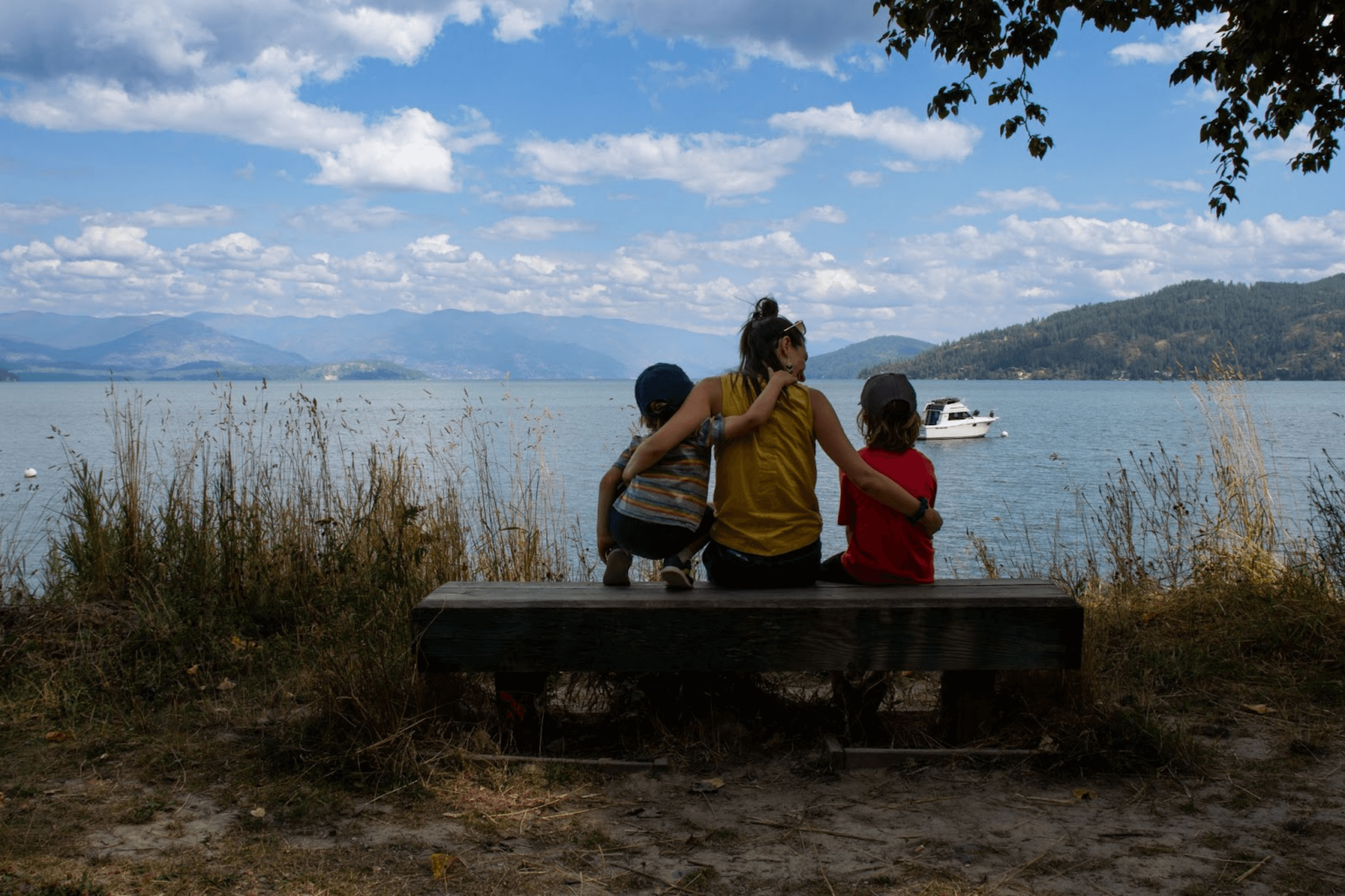 A woman seated between two children on a bench along the Pend d'Oreille Trail, overlooking Lake Pend d'Oreille.