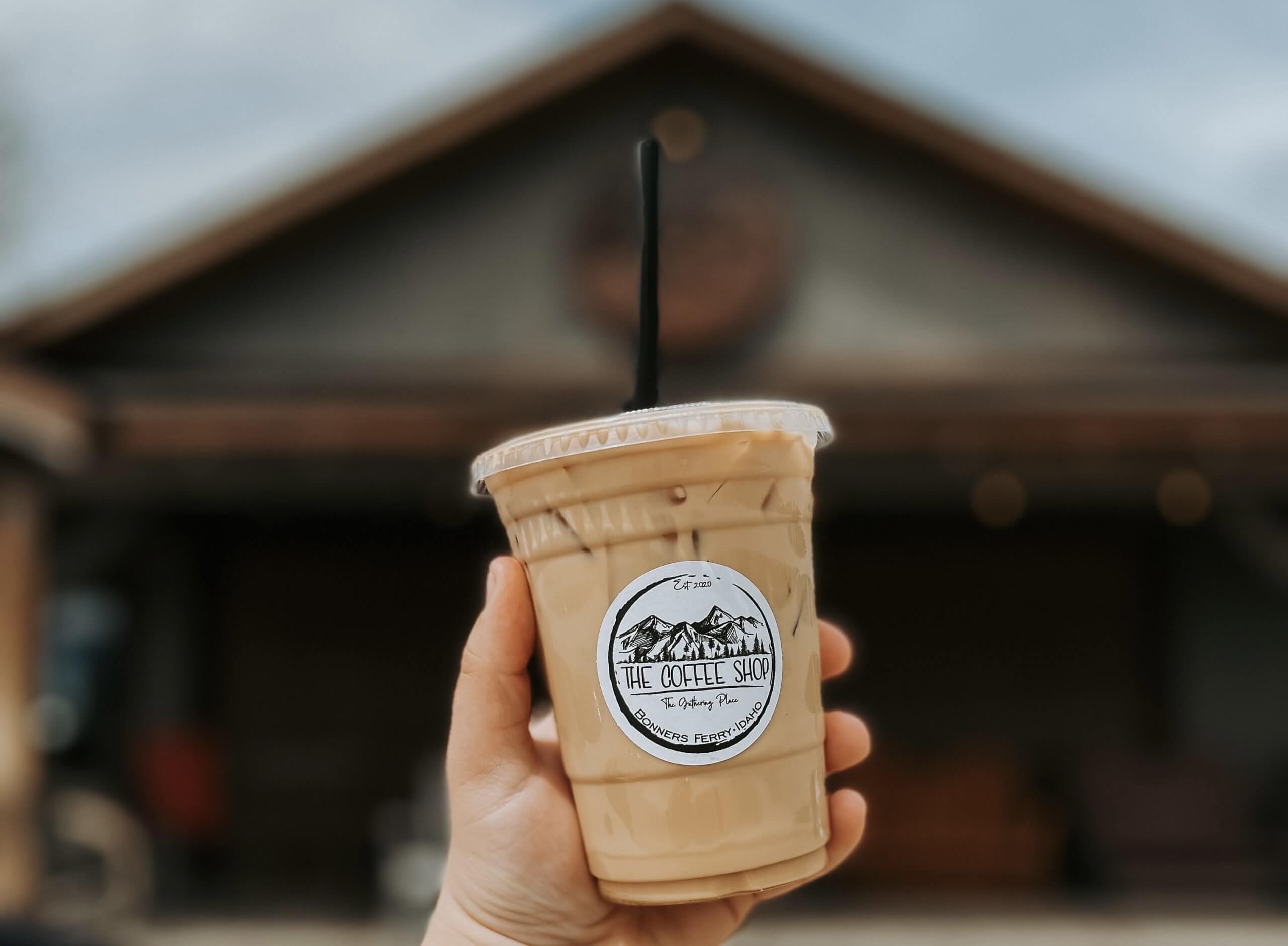 A person's hand holding an iced coffee in front of The Gathering Place.