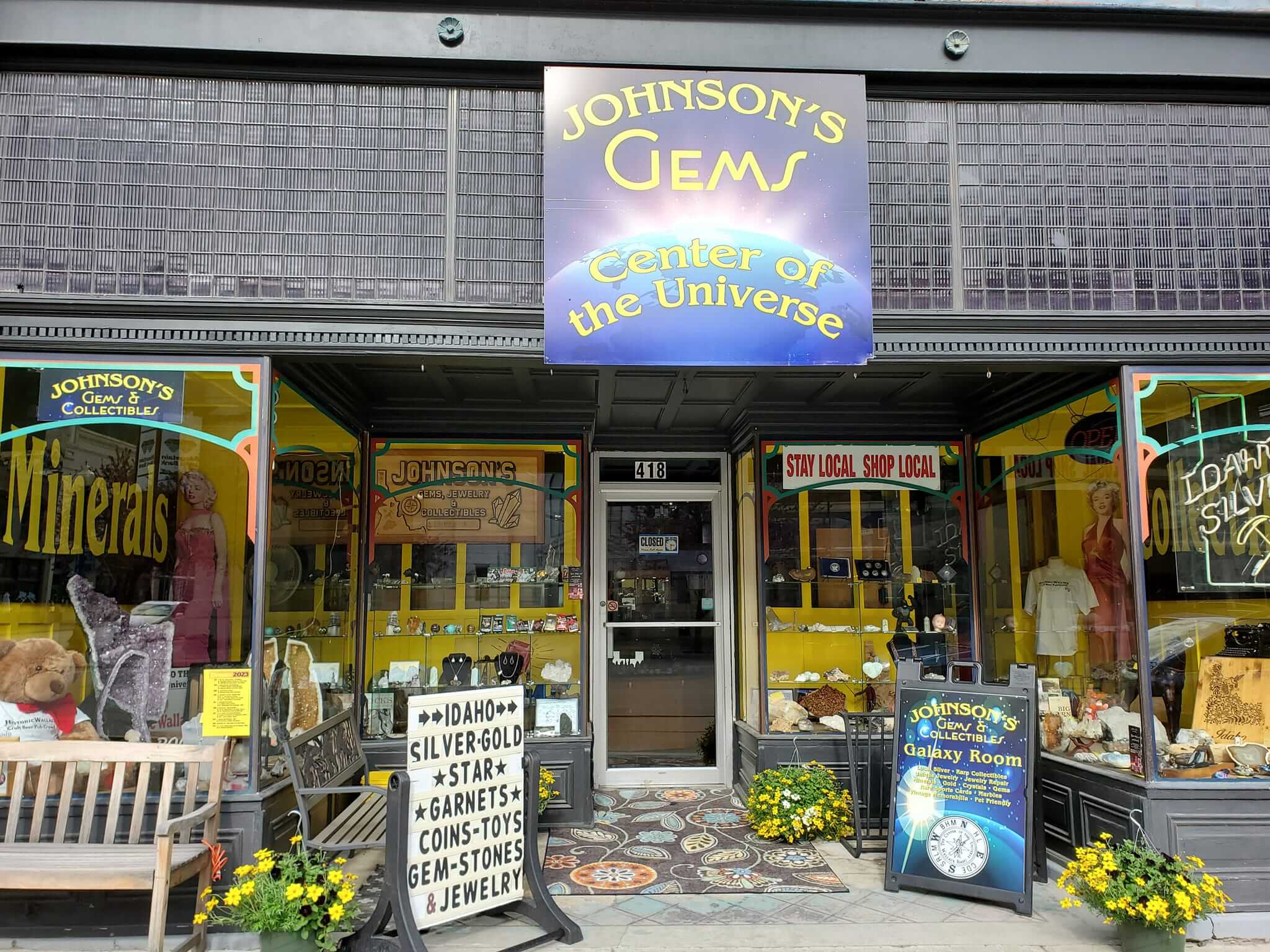 An outside view of the Johnson's Gem's store with several signs out front and items displayed in the windows.