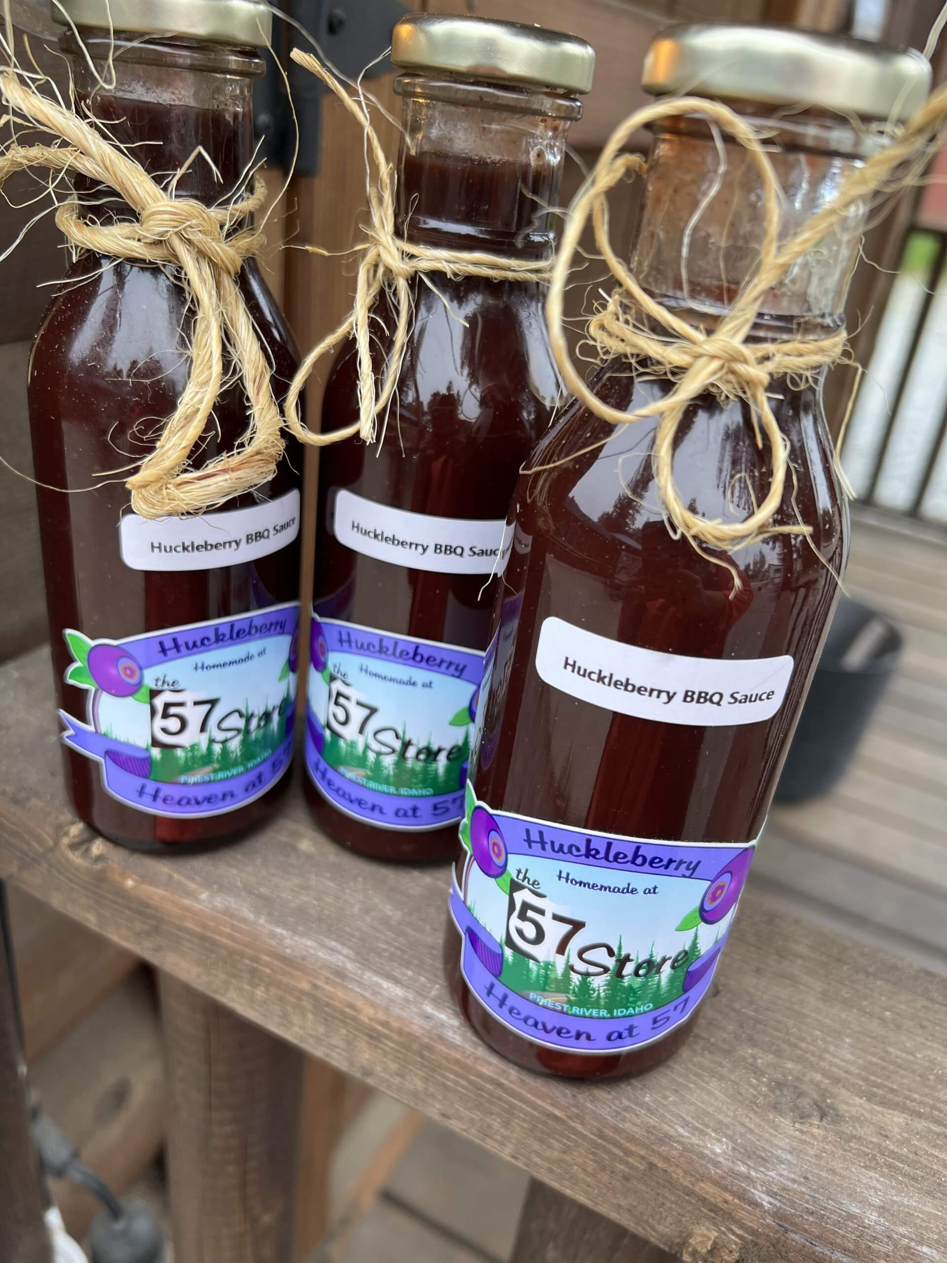 A closeup view of three bottles of huckleberry bbq sauce tied with twine on a wooden table at The 57 Store.