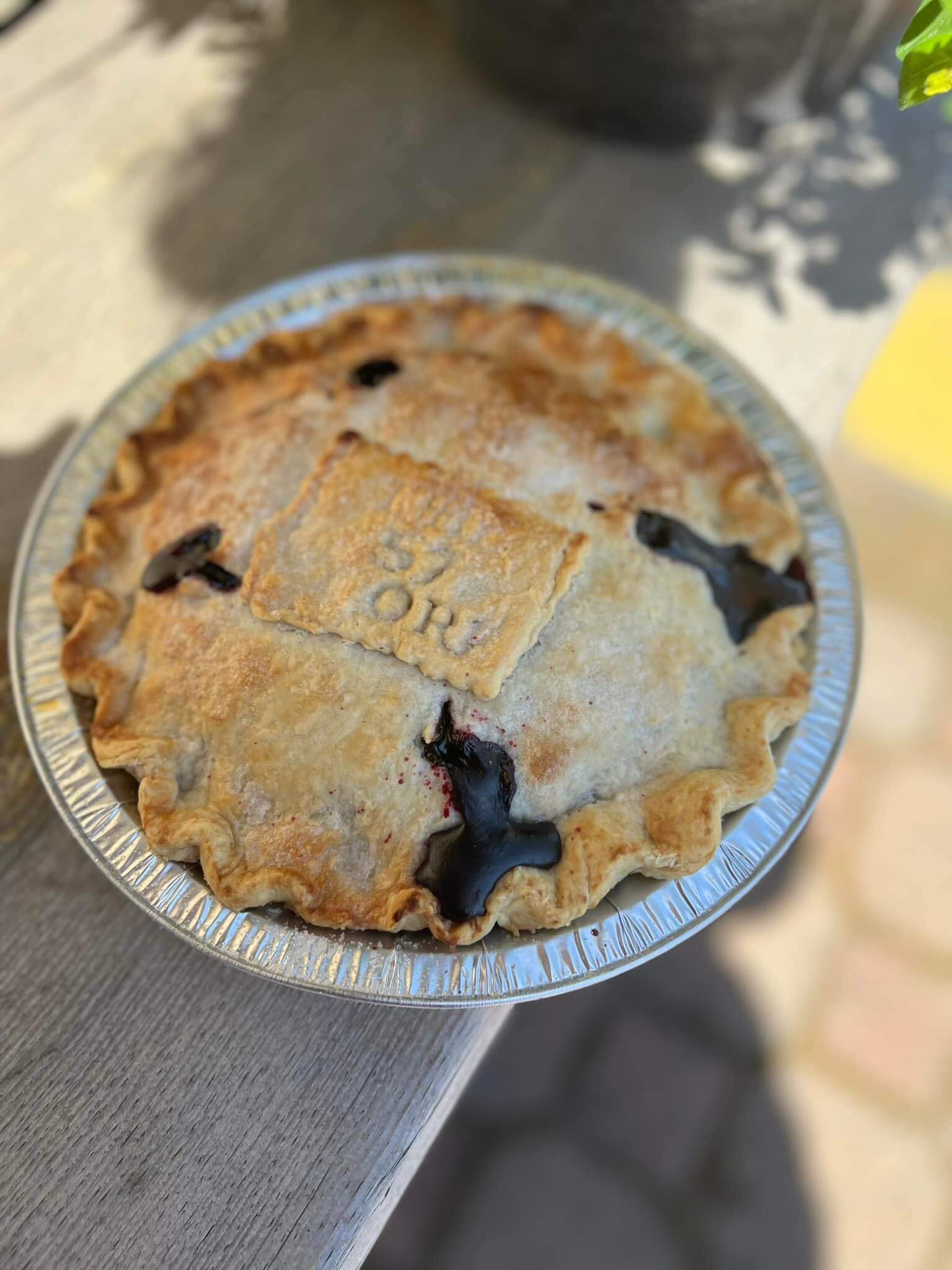 A top view of a huckleberry pie stamped with The 57 Store logo, resting on a wooden table at The 57 Store.