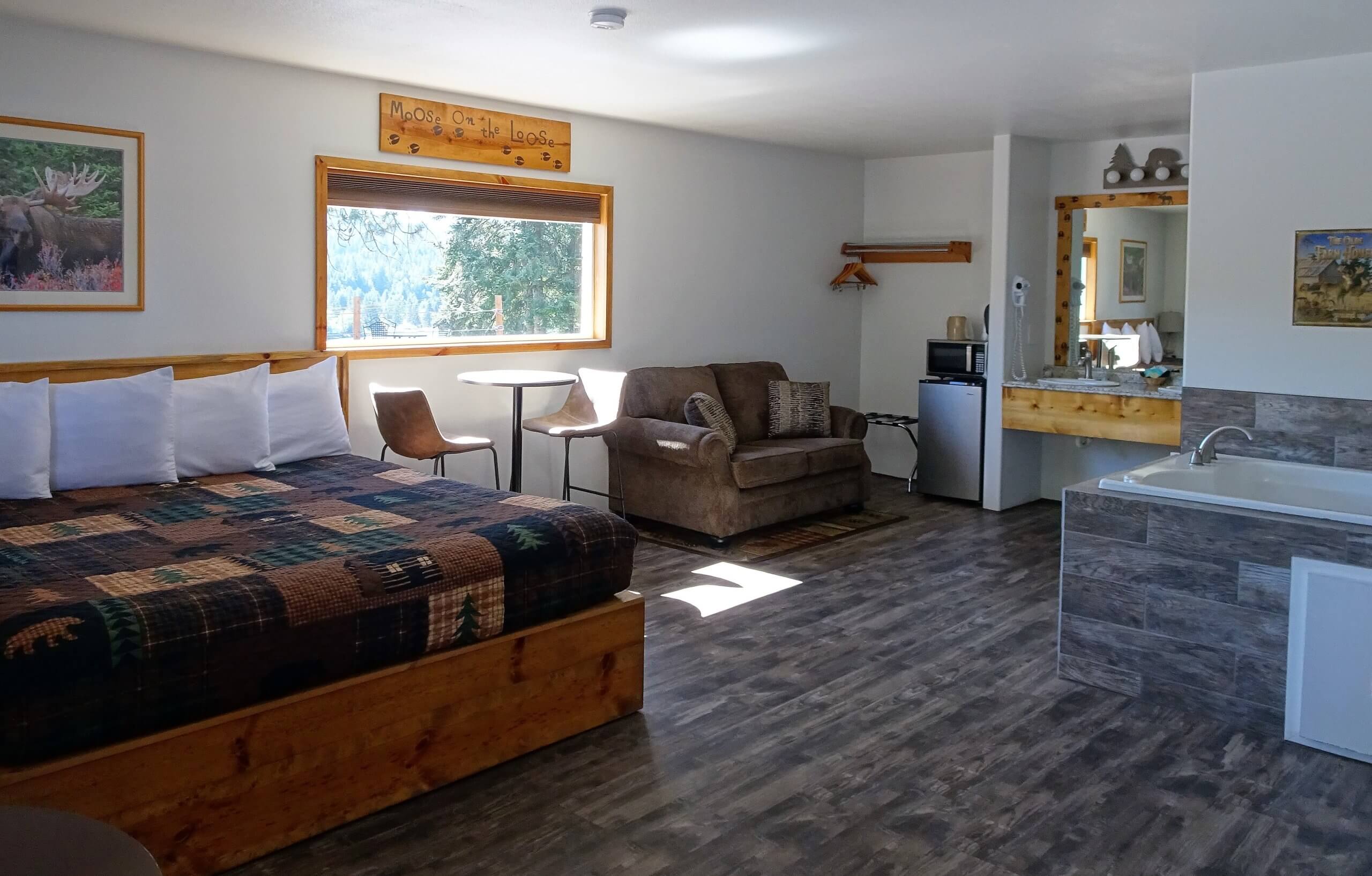 Eagles Nest Motel Spa Suite with a cozy bed, small dining area, loveseat, kitchenette, and jetted tub, featuring rustic wood decor.