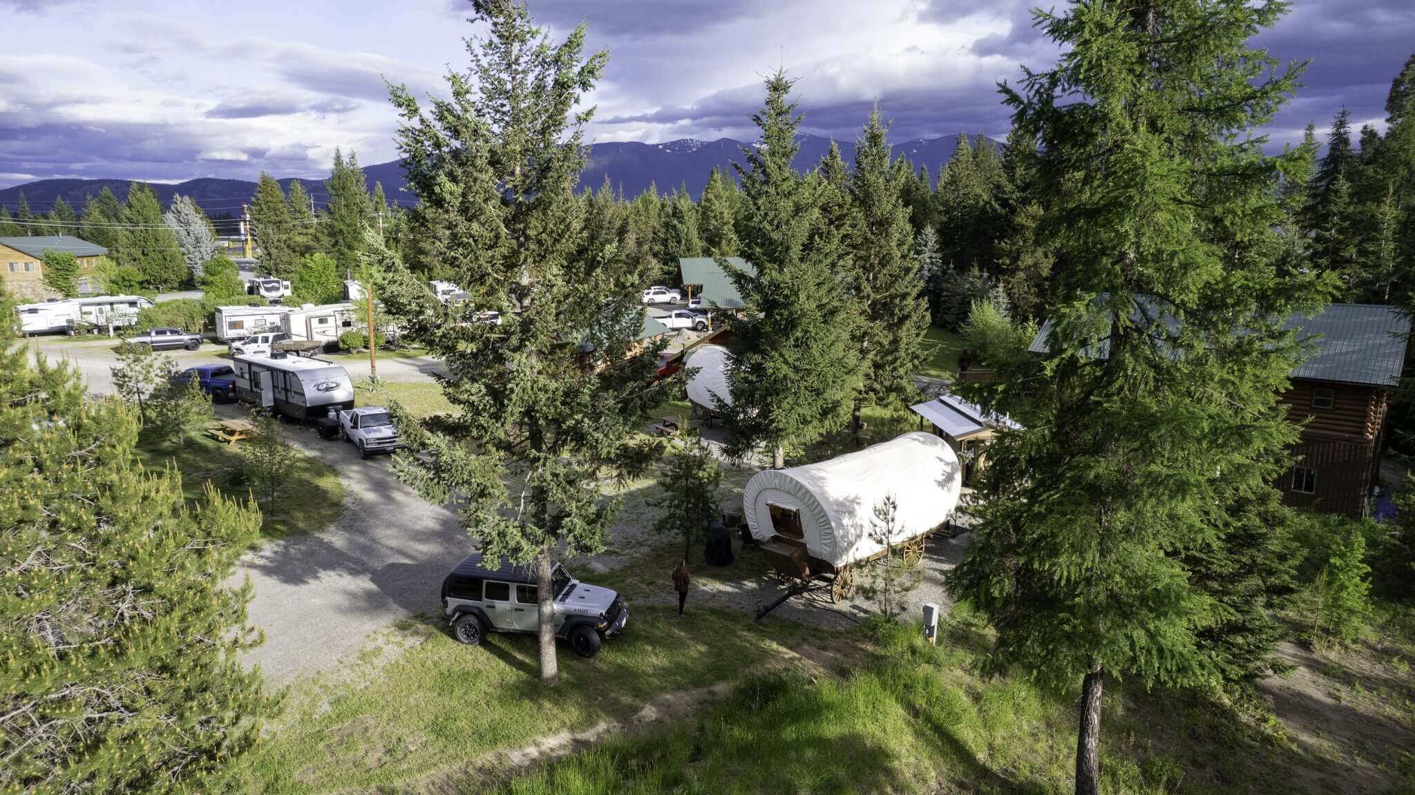 Aerial view of North Haven Campground with RVs, tents, and a covered wagon among pine trees.