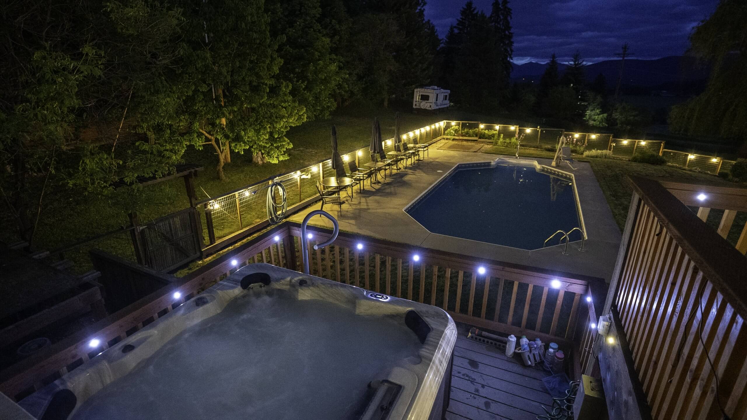 Night view of the lit pool and hot tub area at Northside Schoolhouse, surrounded by trees.