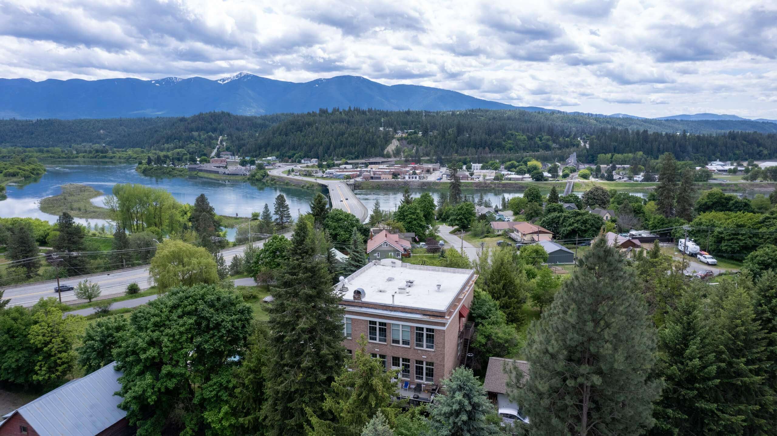 Aerial view of Northside Schoolhouse overlooking the nearby town, river, and distant mountains.