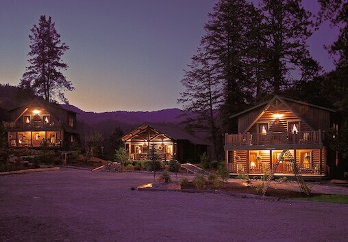 Cabins at Red Horse Mountain Ranch illuminated at dusk, with pine trees and mountain silhouettes in the background.