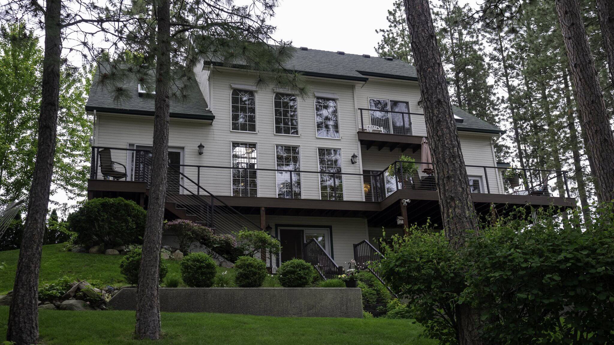 The exterior of River Cove Bed & Breakfast, surrounded by tall pine trees and lush landscaping, with a balcony overlooking the greenery.