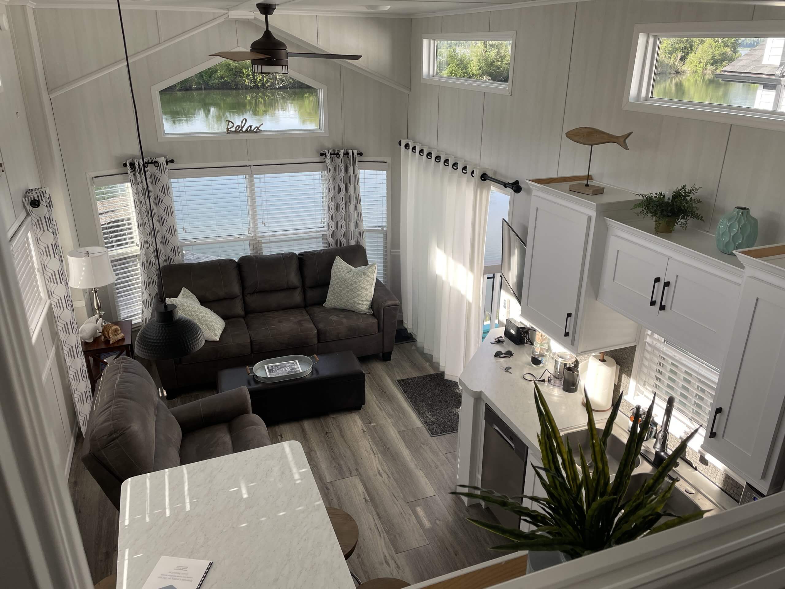 Interior of a tiny house in Saint Maries with a cozy living area featuring a large couch, modern white cabinetry, and large windows offering natural light and views of the water outside.