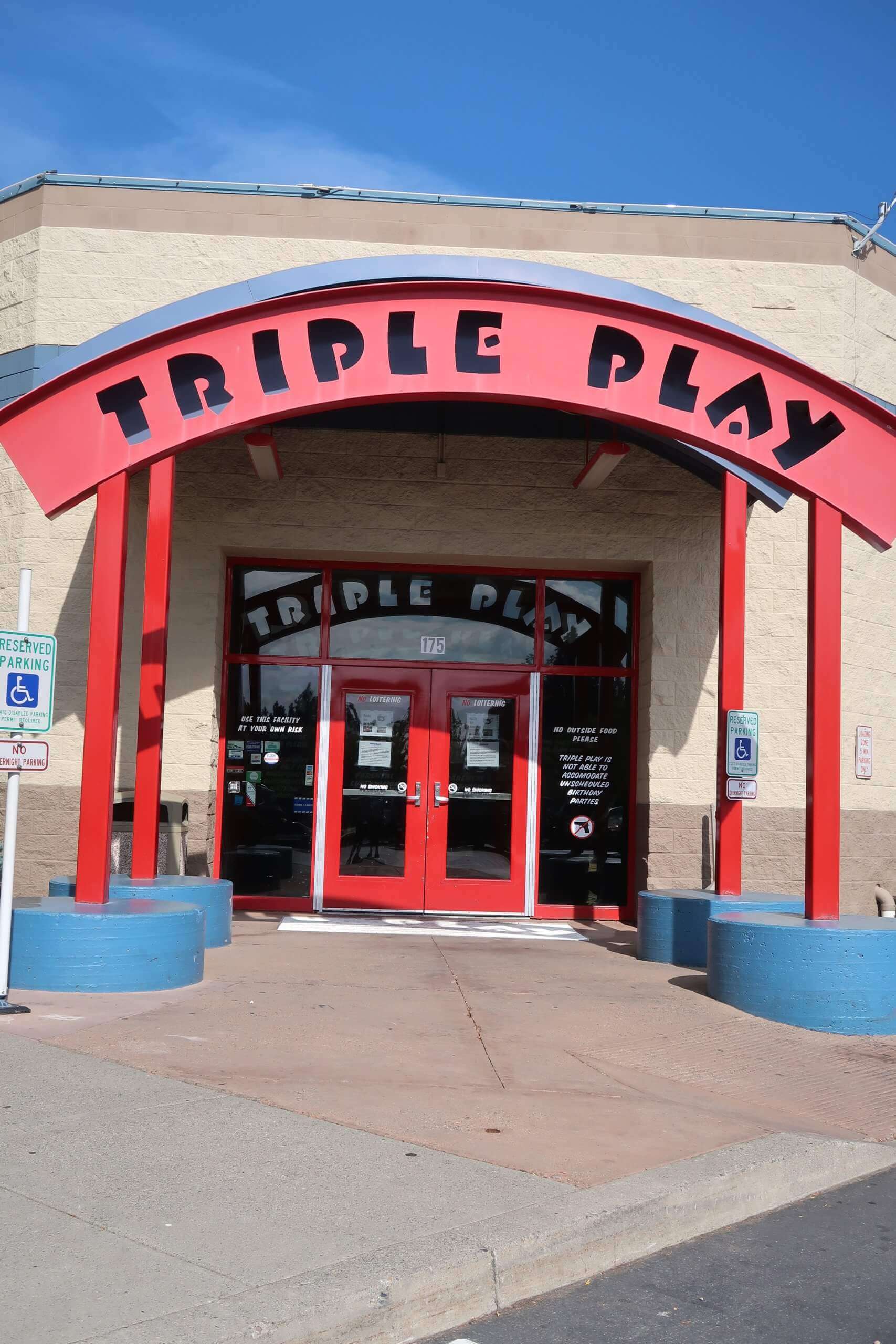 The entrance of Triple Play Resort Hotel & Suites, featuring a bold red archway and bright red doors under a clear blue sky.